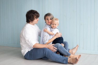 Mutlu bir aile, anne, baba ve oğulları küçük oğulları mavi duvarın yanında otururken evde sarılıyorlar..