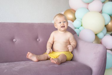 Strabismus gözlü, evde şort giymiş, yerde oturan tatlı bir erkek bebek.