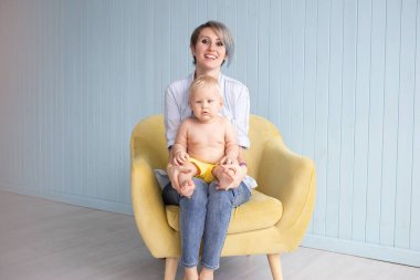 Anne ve oğlu, mavi ahşap bir duvarın yanındaki koltukta otururken, mutlu bir aile.