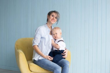 Anne ve oğlu, mavi ahşap bir duvarın yanındaki koltukta otururken, mutlu bir aile.