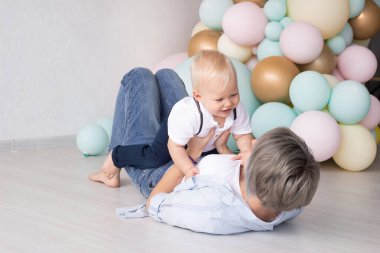 Anne, ilk doğum gününde bebeğiyle renkli balonların arka planında oynuyor..
