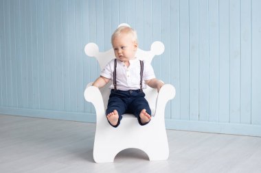İlk doğum gününde evde oturan küçük çocuk taht şeklinde bir sandalyede oturuyor. Takım elbise giymiş, pantolonu ve gömleği var. Aile ve çocukluk kavramı, tatil