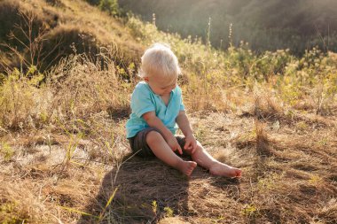 Yazın doğada gün batımında güneş ışınlarıyla çimenlerde oynayan küçük bir çocuk.