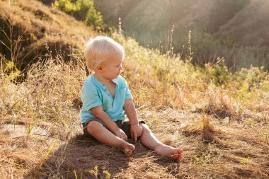 Yazın doğada küçük şirin bir çocuk gün batımında güneş ışınlarıyla çimenlerde oynuyor.