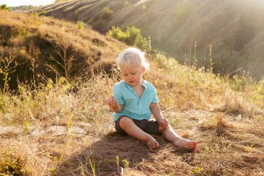 Yazın doğada küçük mutlu bir çocuk gün batımında güneş ışınlarıyla çimenlerde oynuyor.