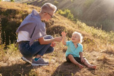 Anne yazın oğluyla birlikte parkta gün batımında güneş ışınlarıyla çimlerin üzerinde oturuyor.
