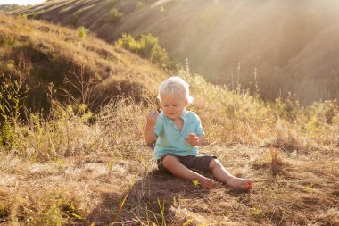 Yazın doğada küçük şirin bir çocuk gün batımında güneş ışınlarıyla çimenlerde oynuyor.