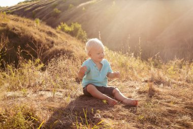 Yazın doğada sevimli tombul bir çocuk gün batımında güneş ışınlarıyla çimenlerde oynuyor.