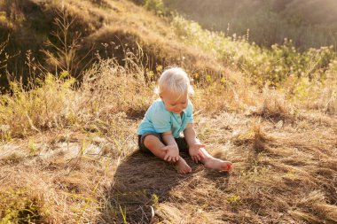 Yazın doğada küçük şirin bir çocuk gün batımında güneş ışınlarıyla çimenlerde oynuyor.