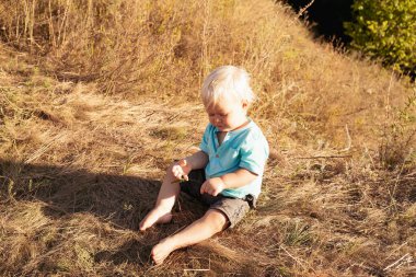 Yazın doğada sevimli tombul bir çocuk gün batımında güneş ışınlarıyla çimenlerde oynuyor.