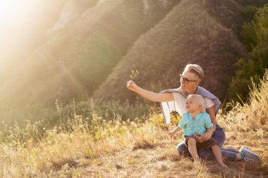 Anne ve oğlu yazın doğada oynuyorlar çimenlerde oturuyorlar gün batımında günbatımında yeşil tepelerin yakınında.