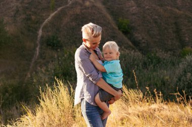 Anne ve oğlu yazın doğanın tadını çıkarıyorlar. Yeşil tepelerin yakınlarındaki günbatımında güneş ışığıyla çimlerin üzerinde.
