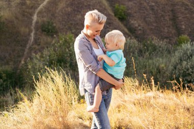Anne ve küçük oğlu yazın güneşin batışında yeşil tepelerin yakınında güneşin tadını çıkarıyorlar.