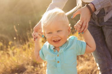 Yazın doğada küçük bir çocuk gün batımında güneş ışığıyla çimlerin üzerinde annesiyle oynuyor.