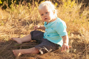 Yazın doğaya bakan Strabismus gözlü bebek gün batımında güneş ışınlarıyla çimenlerde oturuyor.