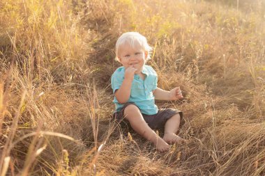 Yazın doğaya bakan Strabismus gözlü bebek gün batımında güneş ışınlarıyla çimenlerde oturuyor.