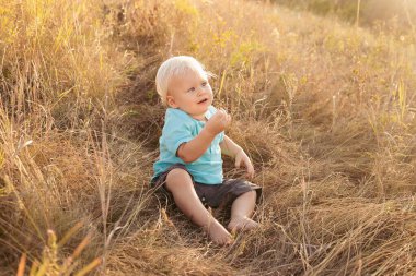 Yazın doğada gün batımında güneş ışınlarıyla çimenlerde oynayan küçük bir çocuk.