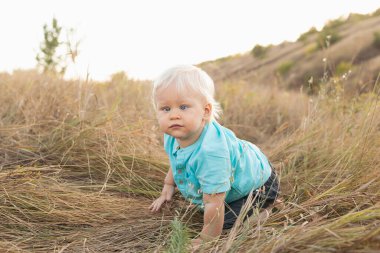Yazın doğaya bakan Strabismus gözlü bebek gün batımında güneş ışınlarıyla çimenlerde oturuyor.