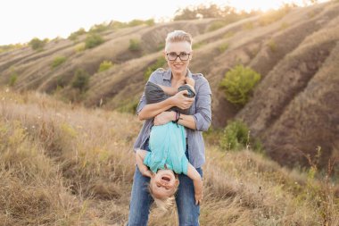 Anne ve küçük oğlu yazın güneşin batışında yeşil tepelerin yakınında güneşin tadını çıkarıyorlar.