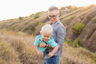 Anne ve küçük oğlu oynuyorlar ve eğleniyorlar yazın günbatımında yeşil tepelerin yakınında.