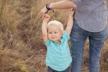 Strabismus gözlü küçük çocuk ve anne yazın ellerini çimlerin üzerinde gün batımında güneş ışınlarıyla tutuyor.