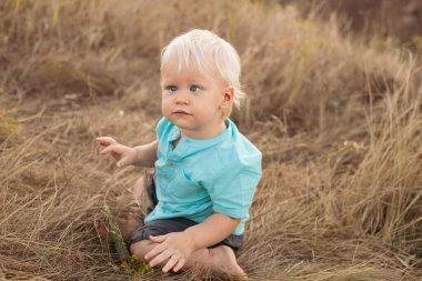 Yazın doğaya bakan, gün batımında güneş ışınlarıyla çimenlerde oturan çocuk.
