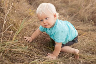 Yazın doğaya bakan, gün batımında güneş ışığıyla çimenlerde oturan çocuk.