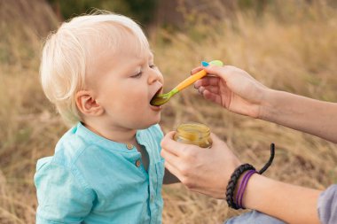 Anne küçük bebeğini kaşıkla kavanozdan püre ile besler.