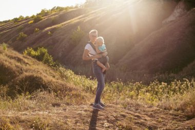 Annem yazın gün batımında güneş ışığıyla çimenlerde askı içinde bebek taşır.