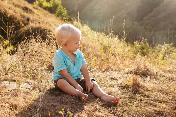 Yazın doğada küçük şirin bir çocuk gün batımında güneş ışınlarıyla çimenlerde oynuyor.