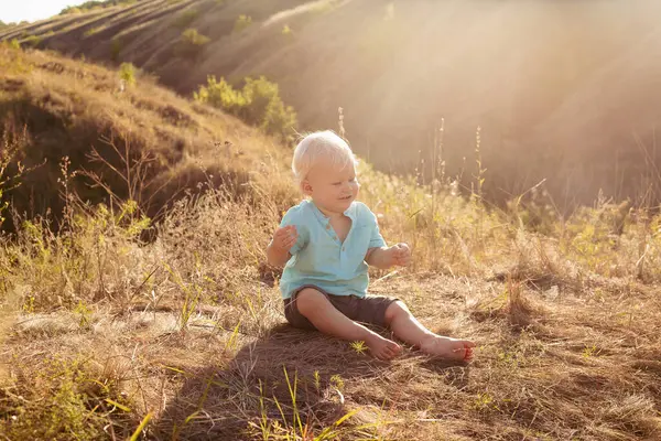 Yazın doğada sevimli tombul bir çocuk gün batımında güneş ışınlarıyla çimenlerde oynuyor.