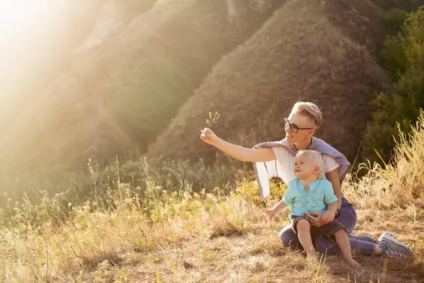 Anne ve oğlu yazın doğada oynuyorlar çimenlerde oturuyorlar gün batımında günbatımında yeşil tepelerin yakınında.