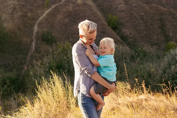 Anne ve oğlu yazın doğanın tadını çıkarıyorlar. Yeşil tepelerin yakınlarındaki günbatımında güneş ışığıyla çimlerin üzerinde.