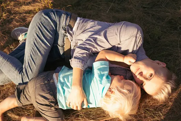 Mutlu anne ve küçük oğlu çimenlerde yatar ve yazın gün batımında güneş ışınlarıyla sarılırlar.