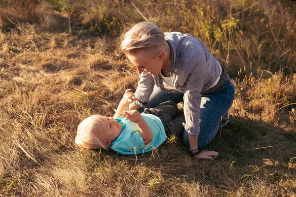 Anne ve küçük oğlu gün batımında güneş ışınları eşliğinde çimenlerde uzanıp oynaşıyorlar.