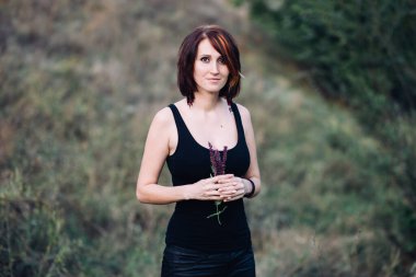 Doğada, günbatımında yeşil tepelerin yakınında elinde çiçeklerle gezen Boho hippi kadın.