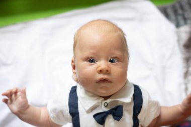 Beyaz gömlek ve papyon giymiş, Strabismus gözlü yeni doğmuş erkek bebek evde.