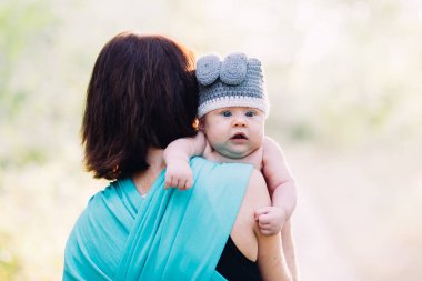 Genç anne oğlunu ellerinin arasında tutuyor, yazın güneş ışığında dışarıda.