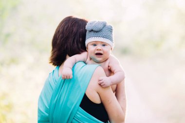 Genç anne oğlunu ellerinin arasında tutuyor, yazın güneş ışığında dışarıda.