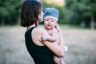 Genç hippi anne bebeğini ellerinin arasında tutuyor, yazın güneş ışığında dışarıda.