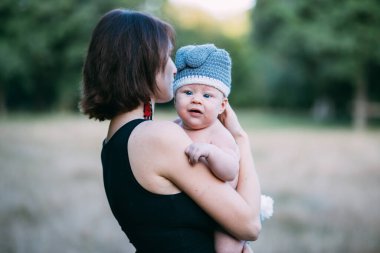 Genç hippi anne bebeğini ellerinin arasında tutuyor, yazın güneş ışığında dışarıda.