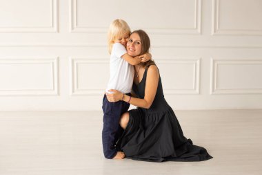 Mutlu anne ve küçük bebeği beyaz duvarın yanında yerde kucaklaşıyorlar. Annelik, şefkat