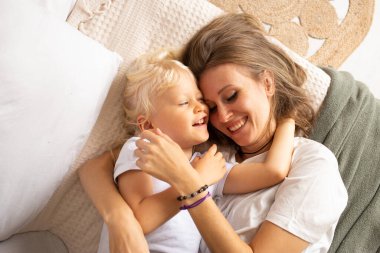 Mutlu anne ve küçük oğlu evde yatakta sarılıyorlar. Annelik, şefkat