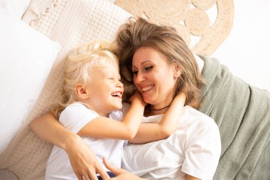 Mutlu gülümseyen anne ve küçük oğlu evde yatakta sarılıyorlar. Annelik, şefkat