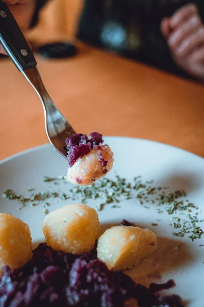 A woman is holding a fork with potatot dumpling and cabbage