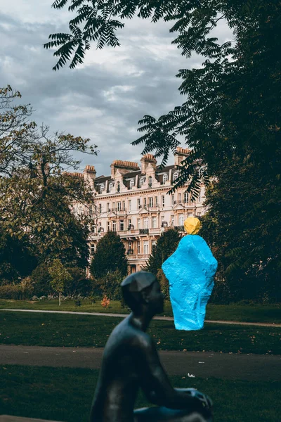 Mimari heykeller, ağaç ve bulutlu gökyüzü ile kasvetli Londra parkı.