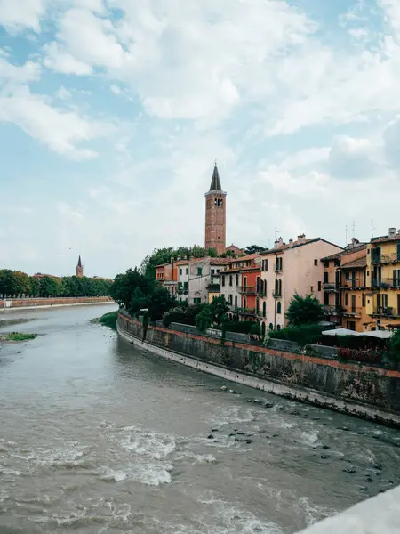 Adige nehri Verona 'nın içinde dolanıyor, canlı yüzlü büyüleyici binalar ve dağınık bulutlu mavi gökyüzünün altında bir çan kulesi sergiliyor..