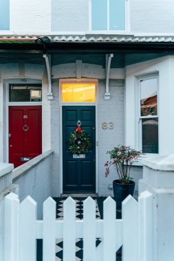 A warm glow emanates from the door of a charming house adorned with a festive wreath. The surroundings show a friendly neighborhood atmosphere during twilight. clipart