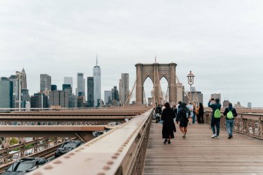 Ziyaretçiler Brooklyn Köprüsü 'nde sakin bir yürüyüş yaparak sonbahar sezonunda bulutlu bir gökyüzünün altında New York şehrinin gökyüzünün muhteşem manzarasını izliyorlar..