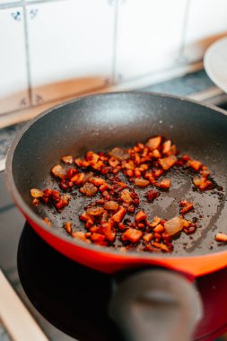 Chopped pieces of vegetables and meat are sizzling in a frying pan on a stove. The browning mixture highlights the cooking process in a cozy kitchen environment.